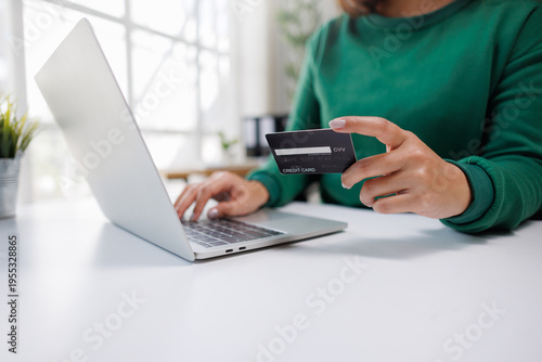 A person is engaged in online shopping, holding a credit card in one hand and typing on a laptop with the other, showcasing modern digital transaction habits.
