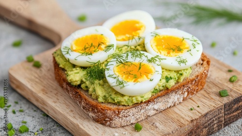 Toasted bread topped with creamy avocado spread and halved soft-boiled eggs, garnished with fresh dill on a wooden board.