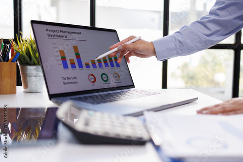 This image showcases a person analyzing a project management dashboard with charts and graphs, emphasizing workflow efficiency and task progress in a corporate setting.