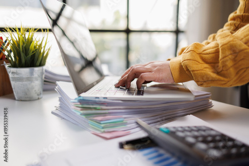 Foto A close-up of a workspace reveals a person typing on a laptop amidst organized stacks of papers, showcasing productivity in a modern office environment