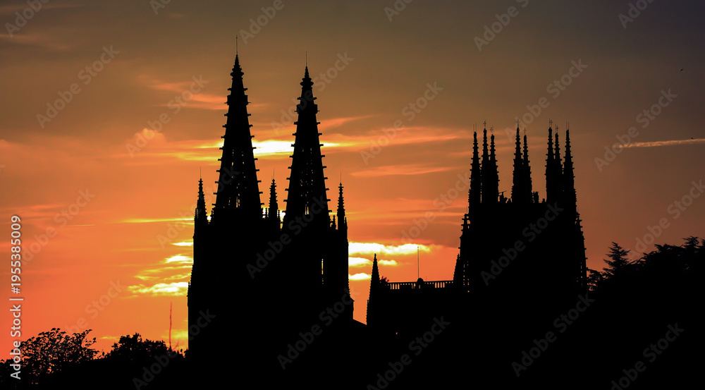 Naklejka premium Silhouette of a gothic cathedral with spires against a fiery orange sunset.