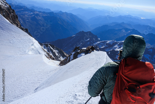 Mountaineer in rope team with crampons taking a picture with his smartphone of mountain glacier panorama in summer on Parrotspitze in Pennine Alps, Italy