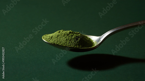 A close-up view of vibrant green powder on a metallic spoon, casting a distinct shadow on a deep forest-green background, highlight health concept