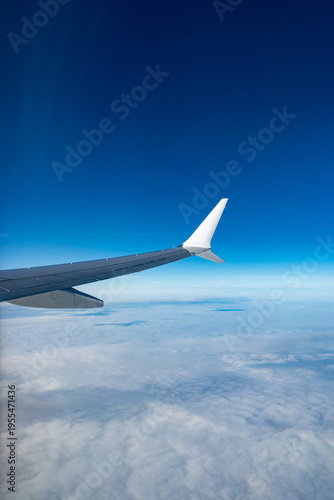 Airplane wings extend above white clouds, providing clear view of  atmospheric layers and sense of altitude during the flight, air transportation