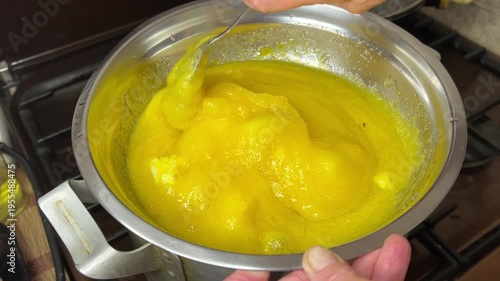 Horizontal side view video of melting ingredients (honey, butter and others) in a double boiler while stirring mixture for honey cake preparation