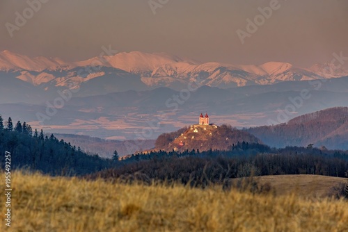 Scenic view of Calvary hill in Banska Stiavnica, Slovakia, with dramatic sunset light and mountain landscape in background. Historic baroque pilgrimage site surrounded by nature.