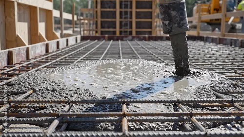 A construction worker pours concrete onto a rebar grid on a building site in a video