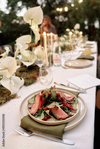 Konstfotografi Romantic outdoor dining scene featuring a candlelit table, soft lights, and a plated salad with greens and meat