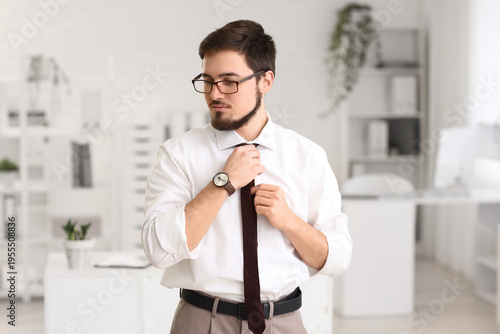 Portrait of handsome businessman adjusting his necktie in office
