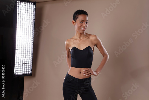 Smiling black woman with short hair posing in professional photo studio with lighting equipment