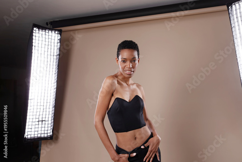 Smiling black woman with short hair posing in professional photo studio with lighting equipment