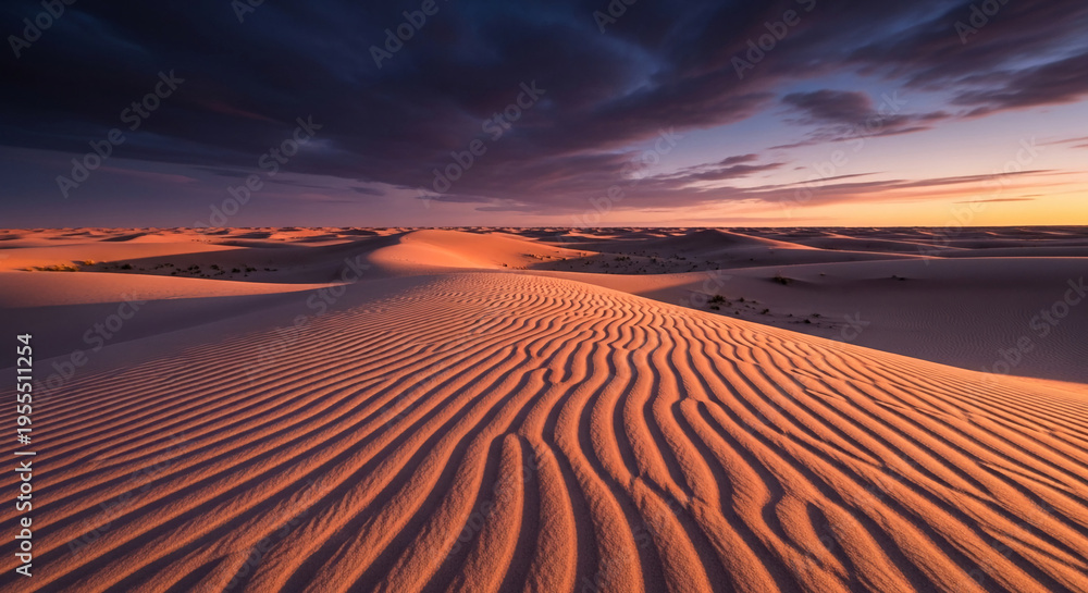 Naklejka premium Vast desert dunes with rippled sand texture under a dramatic sunset sky, symbolizing solitude and natural beauty. Ample free space for text or banner