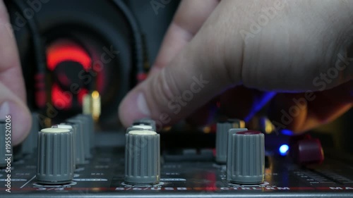 Sound engineer hands adjusting knobs and faders on audio mixer in recording studio.