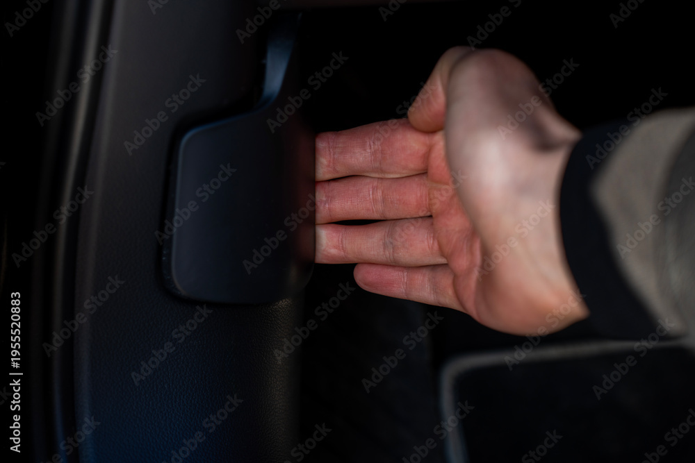 Naklejka premium Driver hand pulling hood release lever under steering column on car dashboard, unlocking engine compartment from inside vehicle interior.