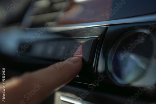 Finger presses hazard warning light button on car dashboard, activating emergency signal system in vehicle interior.