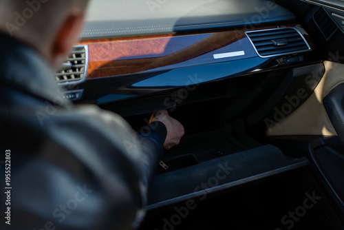 Hand reaching into open glove compartment in car dashboard, interior detail with storage space and trim panel, automotive cabin in daylight.