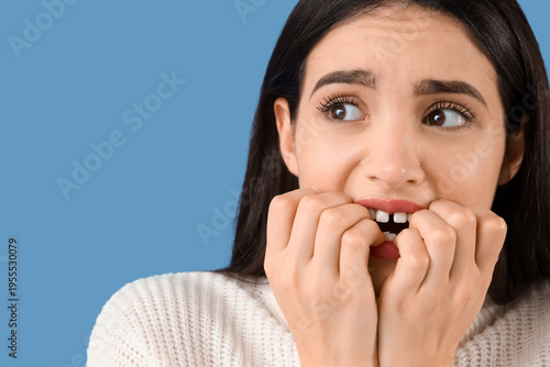 Valokuva Anxious young woman biting nails and looking worried on blue background, close u