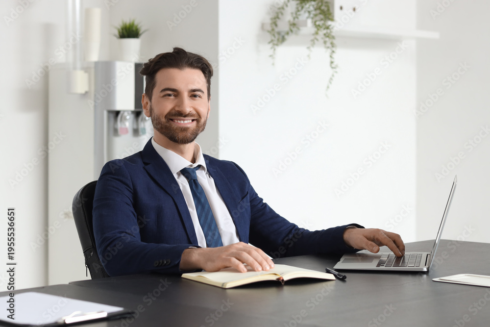 Fototapeta premium Smiling confident businessman working on laptop at desk in modern office, professional male executive portrait with notebook in bright workspace