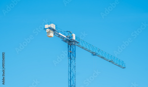 Blue industrial tower crane stands against a clear, vibrant sky. Detailed view of the jib and mast of a construction crane during a bright day