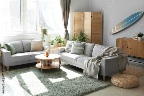 Interior of light living room with surfboard, houseplants and sofas