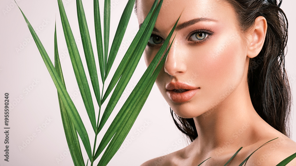 Fototapeta premium Young beautiful woman with green leaves near face. Skin care beauty treatments concept. Closeup girl's face with green leave.