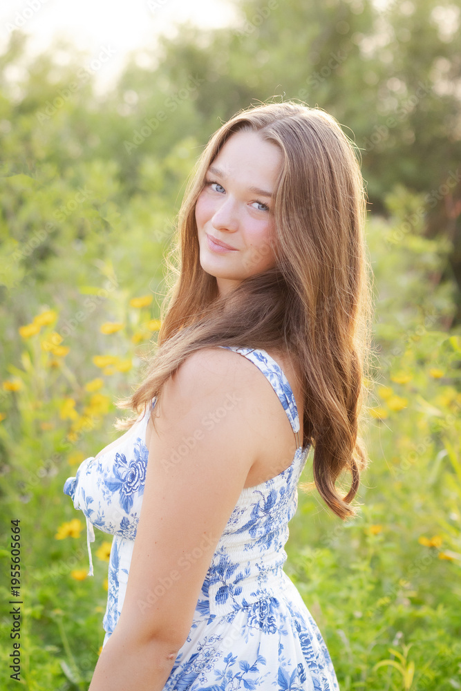 Naklejka premium Sunlit Senior Portrait of Girl in Floral Dress Warm Golden Hour Glow.