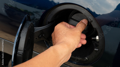 Close up shot of a black plastic fuel gas cap with a ridged edge for easy gripping. Handle to twist the fuel filler cap open or close. A luxurious dark blue car.