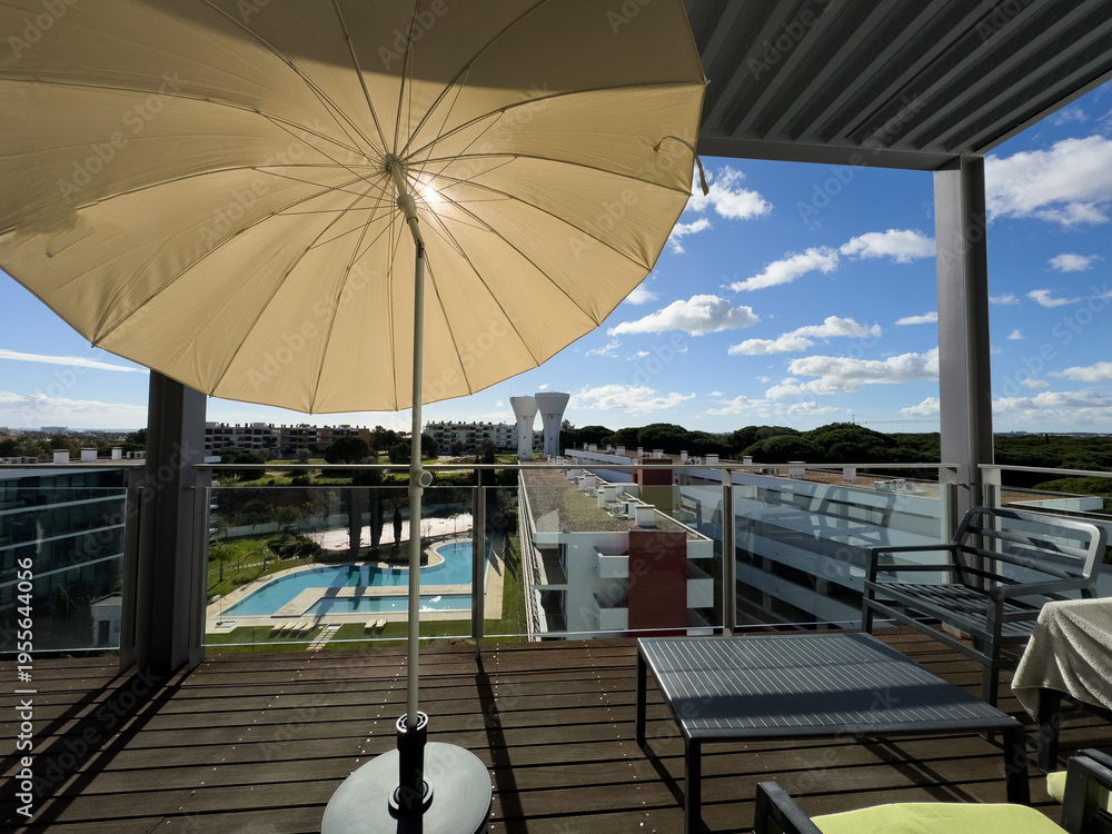 Fototapeta premium An inviting balcony space with comfortable seating, decorative plants, a small table, and a view overlooking modern residential buildings on a cloudy day.