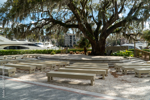 Obraz na płótnie Picturesque outdoor amphitheater beneath a majestic Spanish moss-draped live oak tree, overlooking a vibrant marina filled with luxury yachts and modern waterfront architecture