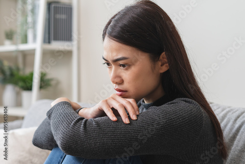 Unhappy anxiety young Asian woman covering her face with pillow on the cough in the living room at home.