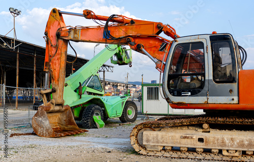 Heavy industrial excavator and green telehandler loader at construction site background