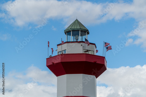 фотографія Iconic Harbour Town Lighthouse in Hilton Head Island, South Carolina, USA, adorned with American flags against a vibrant blue sky, a striking red and white beacon with a distinctive green cap