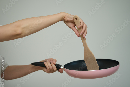 Frying pan in human hands, Cooking concept. Hand holds a pink frying pan by the handle, showing the metallic textured bottom surface.