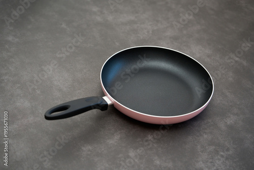 Pink nonstick frying pan on dark surface. Nonstick frying pan with black handle placed on a dark surface, showcasing modern kitchen cookware design.