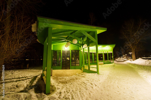 A brightly lit, green, curved pavilion in the snow at night.