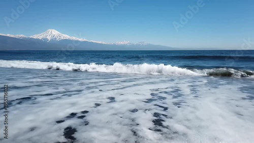Serene Black Sand Beach Meets Ocean Waves with Snow-Capped Mountains Under a Clear Blue Sky