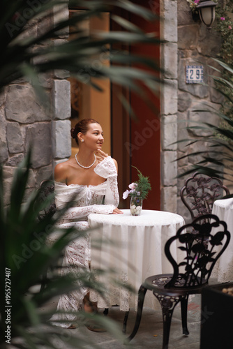 Romantic Woman in Lace Sitting by Rustic Stone Cafe With Floral Decor