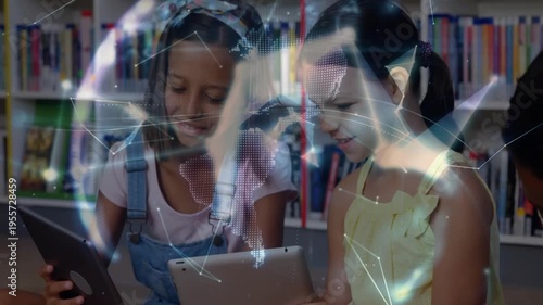 Two girls sitting in library tapping tablets, mesh forming globe between them for learning