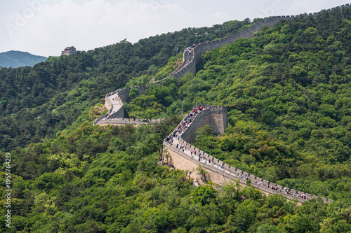 The Great Wall of China winds across the lush green mountains of Badaling under a clear blue sky.