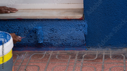 Painting blue wall with roller near window exterior renovation