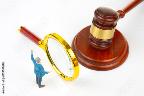 Miniature people using a magnifying glass near a gavel in a legal setting with bright light and clean background