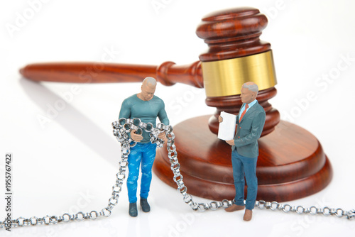 Miniature figures stand near a gavel, one holds chains while another presents a document during a legal scene