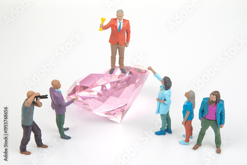Miniature people celebrating around a large pink diamond during a fun creative scene