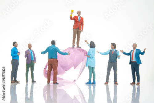 Tableau sur toile Miniature people celebrate on a large gem while one holds a trophy under bright