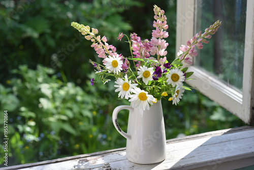 Bouquet of wild flowers in a vase on a wooden window sill. Floral decoration on the window of an old country house, summer cottage.