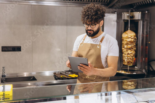 Arab man chef managing a small restaurant business, checking orders and inventory on a digital tablet in the kitchen