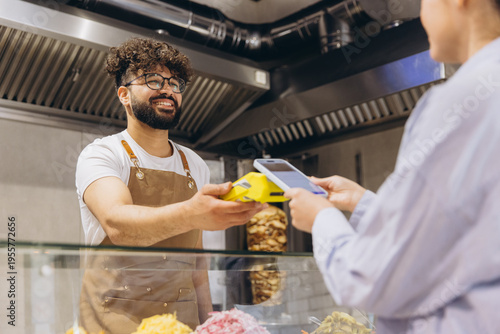 Cuadro en lienzo Man in apron holding payment terminal for customer making contactless transactio