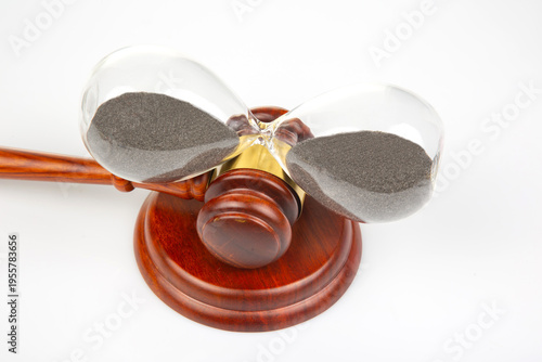 Hourglass and gavel on a wooden table represent time in a legal setting with dark sand in the hourglass marking moments