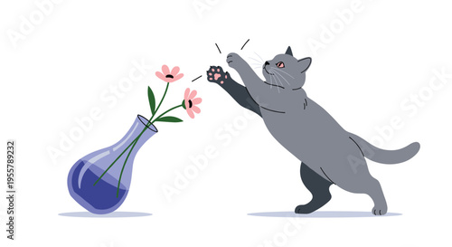Playful grey cat jumps and reaches for pink flowers in a tilted blue glass vase on a plain white background with shadow.