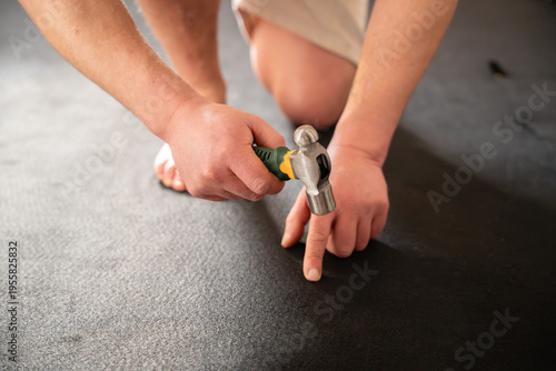 Foto Man accidentally hitting his finger with hammer while fixing flooring underlay d